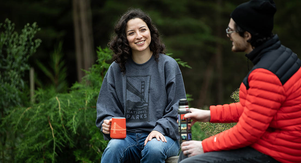Two people talk and hold mugs with parks in the background.