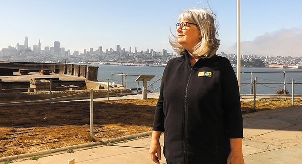 Nicki Phelps stands on Alcatraz Island with a view of San Francisco behind her.