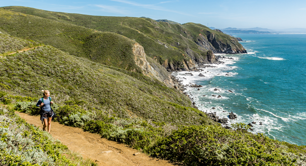 A hiker looks out at scenic view of the pacific coastline from the Coastal Trail in Marin Headlands on a bright sunny day.