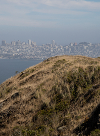 A park visitor runs on the SCA Trail in the Marin Headlands with the San Francisco skyline in background.