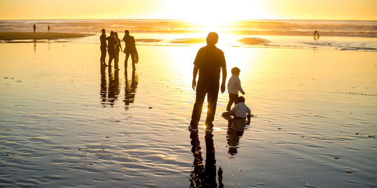 Visitors and families bask in a golden sunset where the water meets the sands of Ocean Beach.