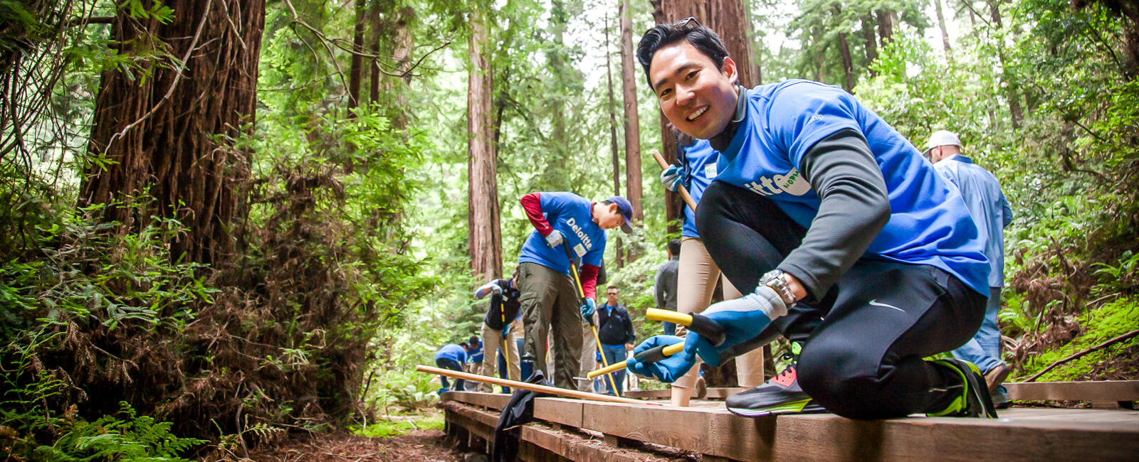 Corporate volunteers smile at the camera while working on Muir Woods trails. Old growth redwood trees fill the background of this historic national parks landmark in the Marin Headlands in the San Francisco Bay Area Golden Gate National Recreation Area.