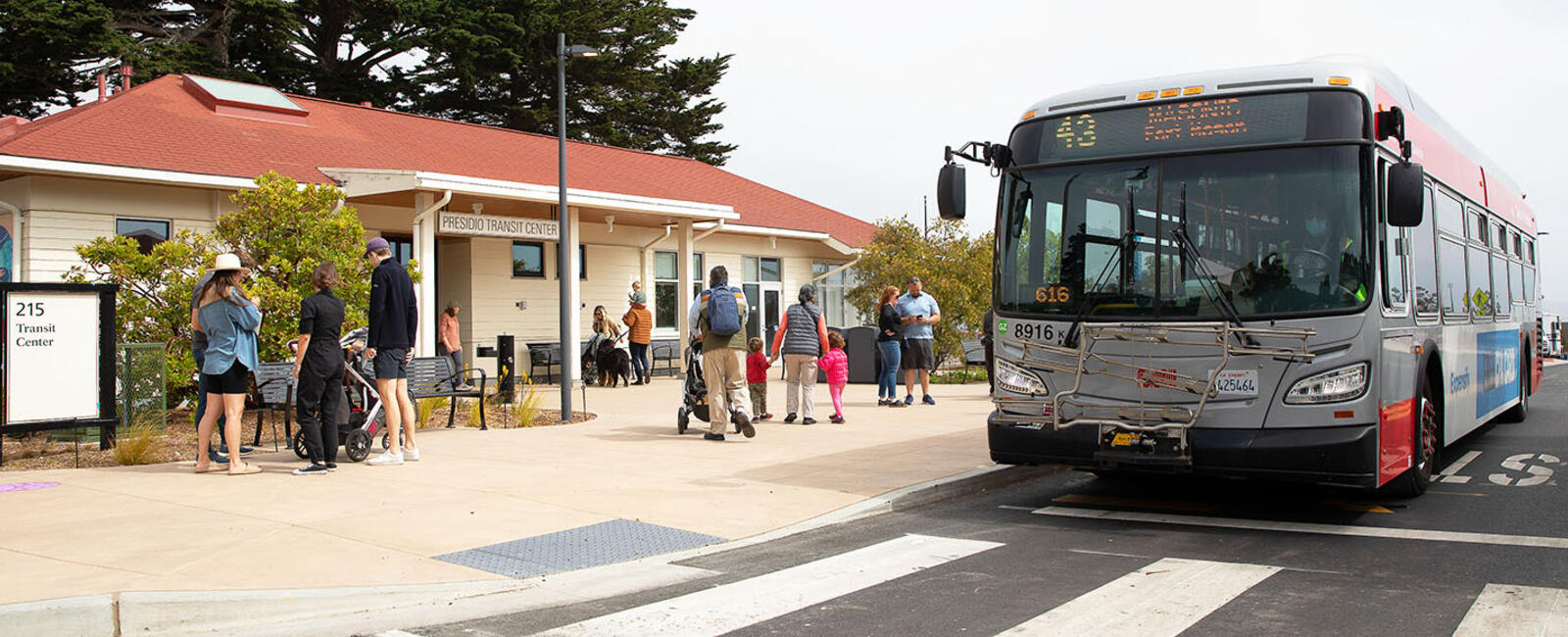 A red and gray San Francisco Muni bus parked at a station in the Presidio