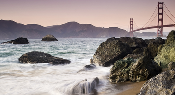 Waves crashing over rocks at Marshall's Beach with Golden Gate Bridge in the background.