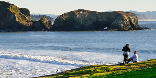 People on a green bluff overlooking the waves of the Pacific Ocean.