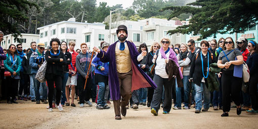 Person in costume leading a crowd of audience members through a park