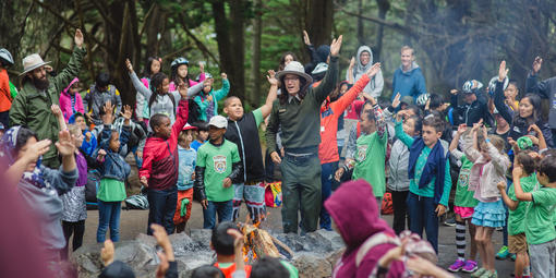 A National Park Service Ranger leads a large group of smiling children in an interactive story