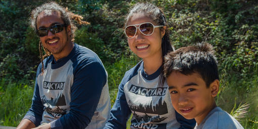 Two adults and a young boy sit together outdoors in bright sun.