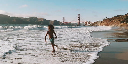 Child plays in the waves with Golden Gate Bridge in background.