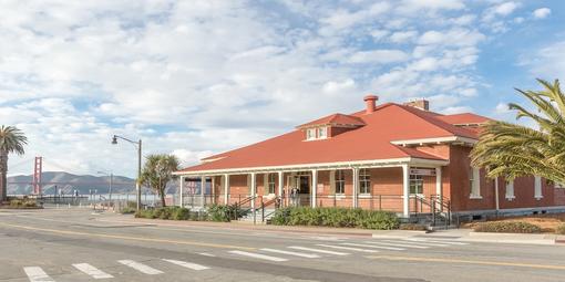 Image of the front of the Presidio Visitor Center with the Golden Gate Bridge in the backgrounr