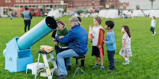 Children watching an astronomer adjust a telescope on the Presidio Main Lawn for stargazing