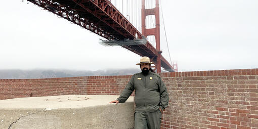 NPS Ranger Erick Cortes stands in front of the Golden Gate Bridge at Fort Point Historic Site.