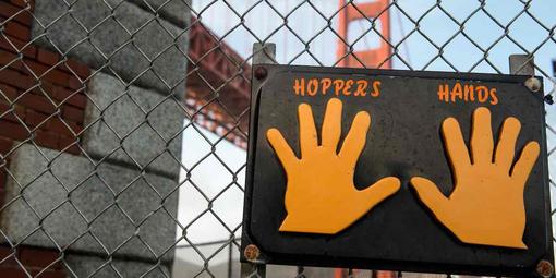 Sign labeled "Hopper's Hands" on a fence with the Golden Gate Bridge behind.