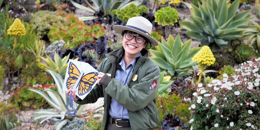 Ranger Rebecca Au poses with a butterfly drawing in a flower field.