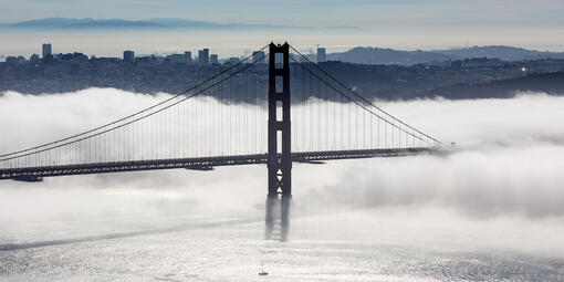 Golden Gate bridge in a layer of fog with a view of San Francisco behind it. 