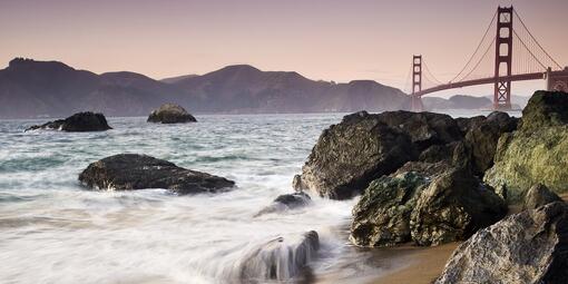 Waves crashing over rocks at Marshall's Beach with Golden Gate Bridge in the background.