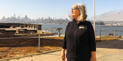 Nicki Phelps stands on Alcatraz Island with a view of San Francisco behind her.