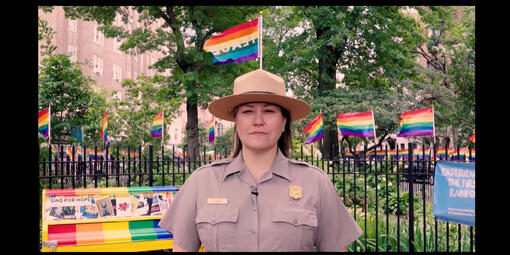 National Park Service Ranger Jamie Adams stands at the Stonewall National Monument with a backdrop of rainbow flags in celebration of Pride Festival.