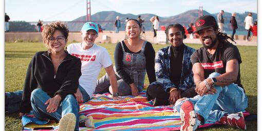 Five people sit on a colorful, striped blanket at Presidio Tunnel Tops