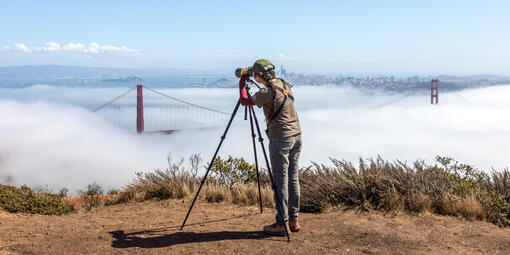 A woman peers through a birding telescope looking over the golden gate bridge and san francisco bay