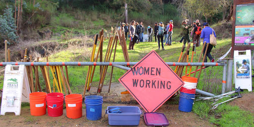 Sign saying "Women Working" with a trail crew in the background.