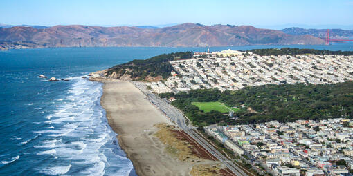 Aerial view of Ocean Beach showing waves lapping against the shore before San Francisco, along with the Golden Gate and Marin Headlands in the background.