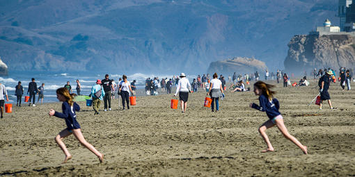Two girls run in foreground of a wide shot of a crowded Ocean Beach.