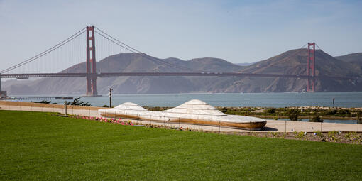 An artistically crafted bench at Presidio Tunnel Tops sits before the Golden Gate Bridge and Marin Headlands in the background.