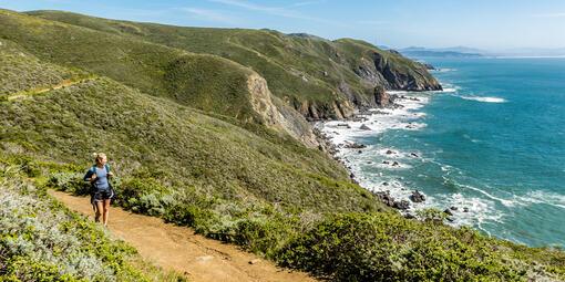 A hiker looks out at scenic view of the pacific coastline from the Coastal Trail in Marin Headlands on a bright sunny day.