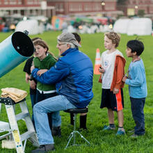 Children watching an astronomer adjust a telescope on the Presidio Main Lawn for stargazing