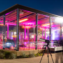 Long exposure photo of an enclosed outdoor picnic area in the Presidio glows with bright pink lights with an astronomy telescope seen in the foreground