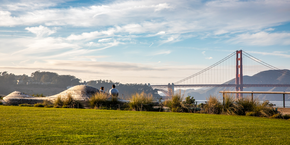 A scenic view of the Golden Gate Bridge seen from the Presidio Tunnel Tops in San Francisco, visitors seen sitting on the iconic wooden park bench.
