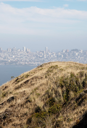 A park visitor runs on the SCA Trail in the Marin Headlands with the San Francisco skyline in background.